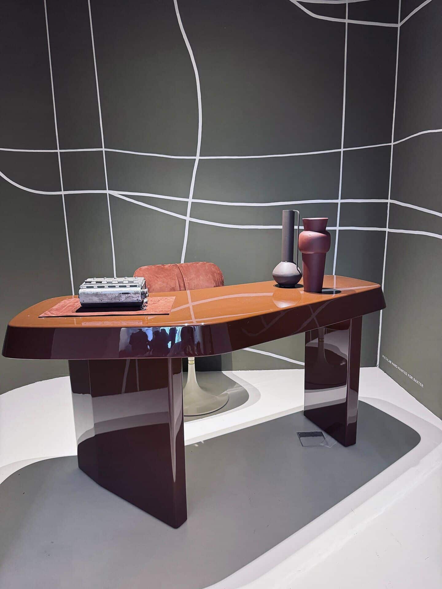 glänzender Schreibtisch in Rostrot vor Akzentwand auf der Designmesse Mailand